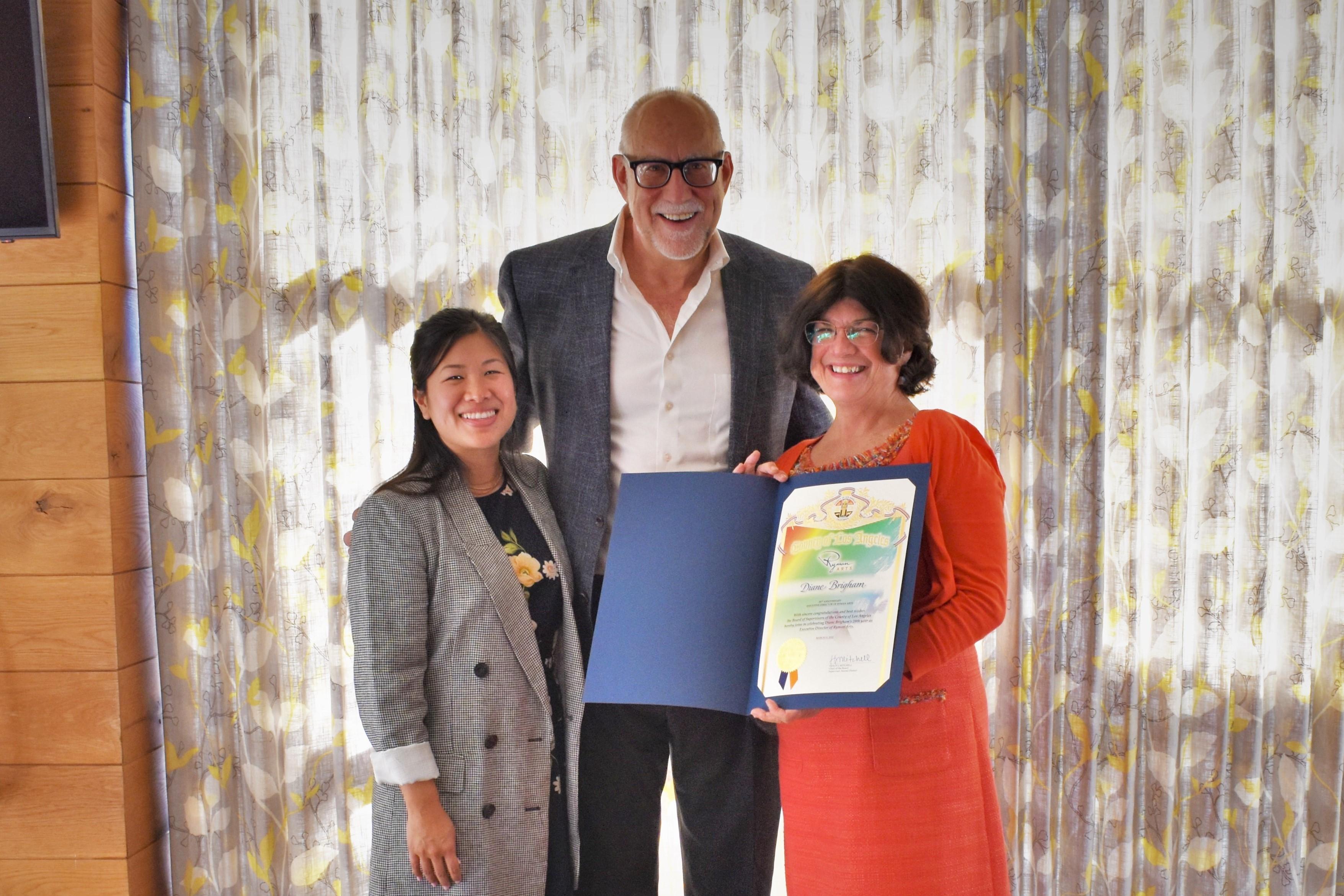 Three people standing with person on the right holding award: Shannon Huang, Phil Hettema, and Diane Brigham (left to right)